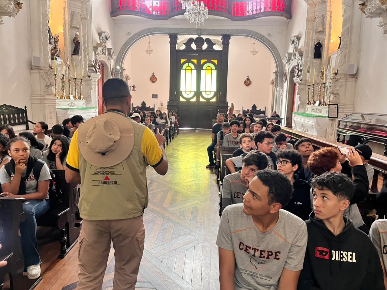 Prudêncio conduzindo estudantes no interior de uma igreja barroca